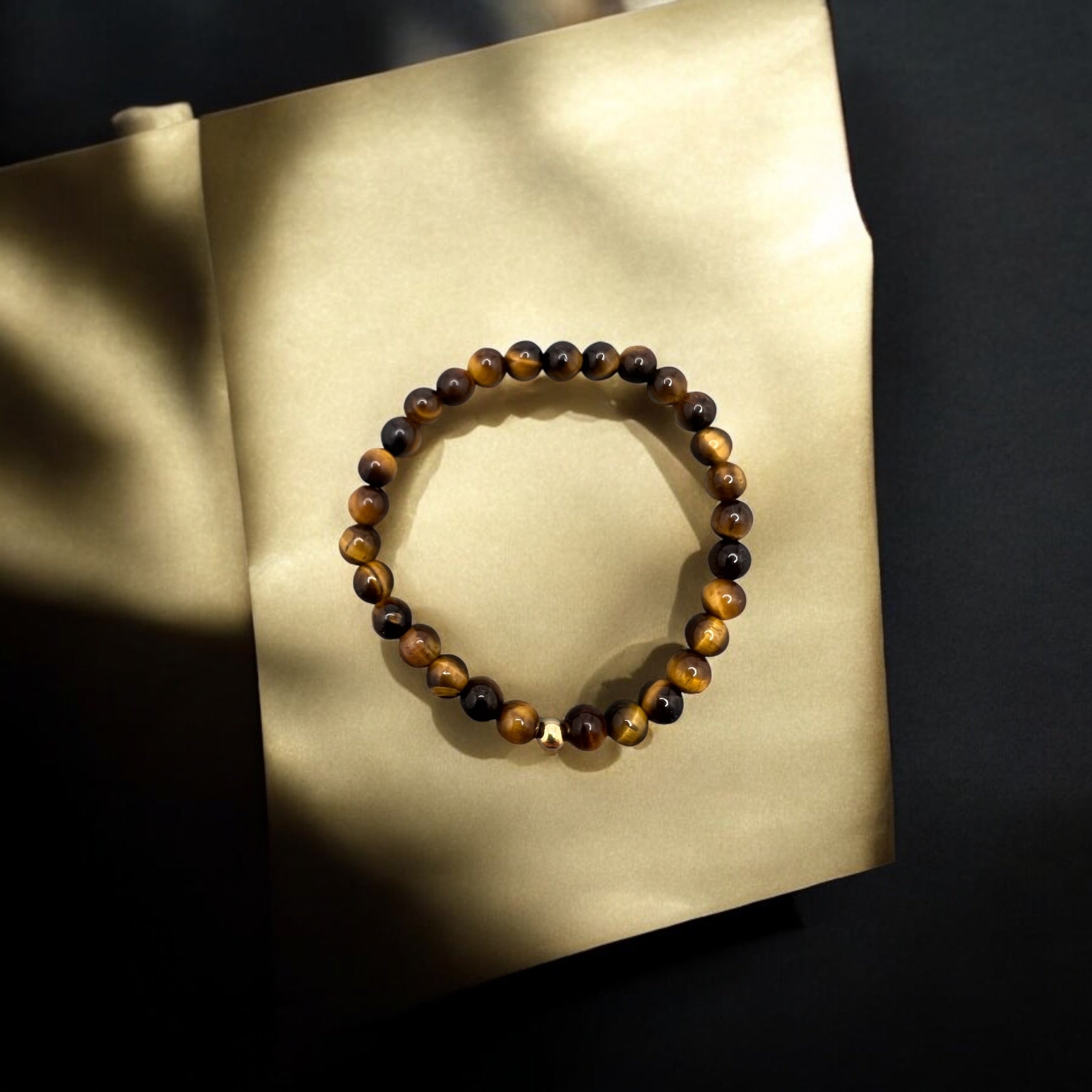 Tigerauge Armband with 6mm round golden-brown tiger eye gemstone beads on an elastic band displayed on beige background, symbolizing courage and willpower