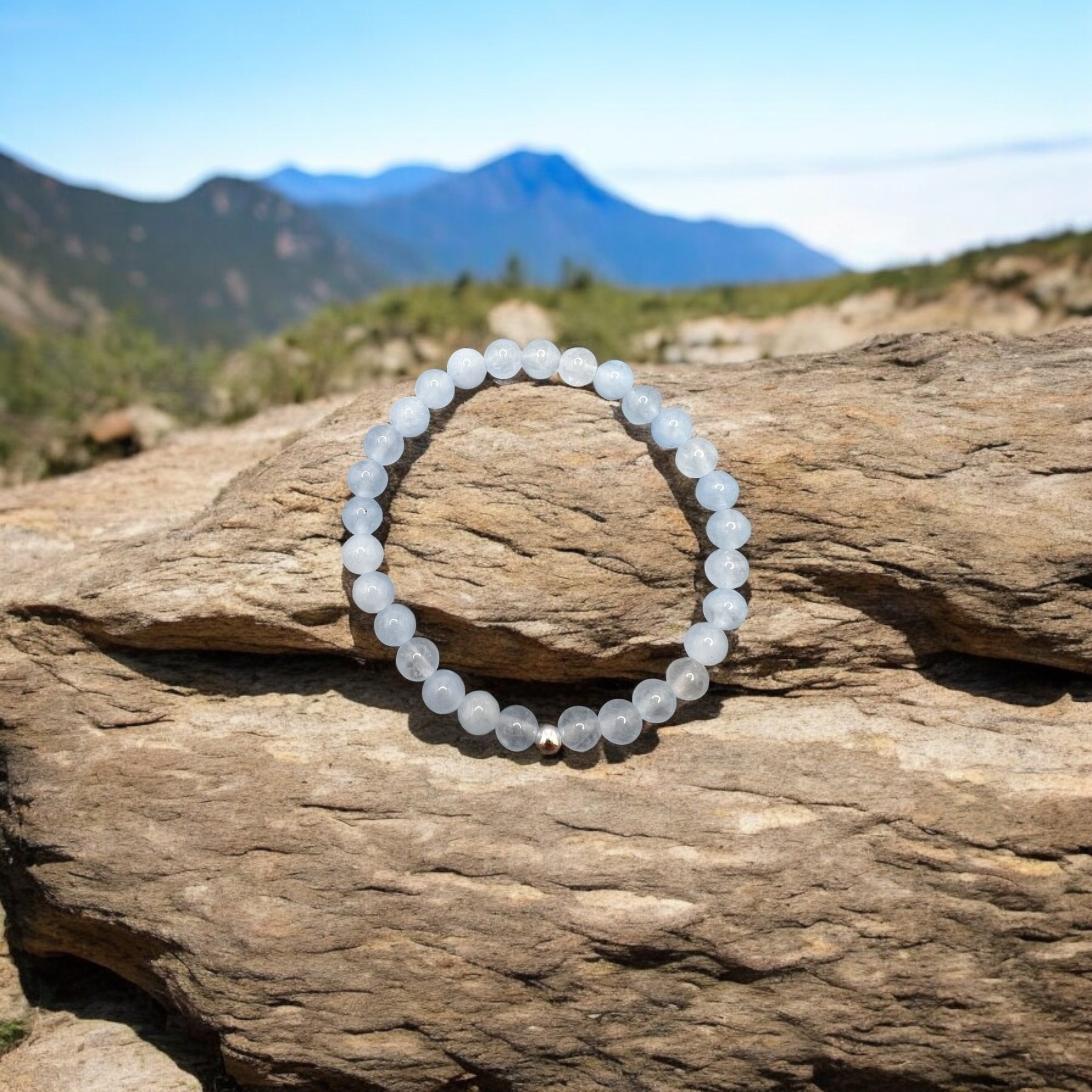 Handgefertigtes Aquamarin Armband aus runden Perlen, symbolisiert Gelassenheit und klare Kommunikation, wasserfest und robust, fotografiert auf Felsen vor Berglandschaft.