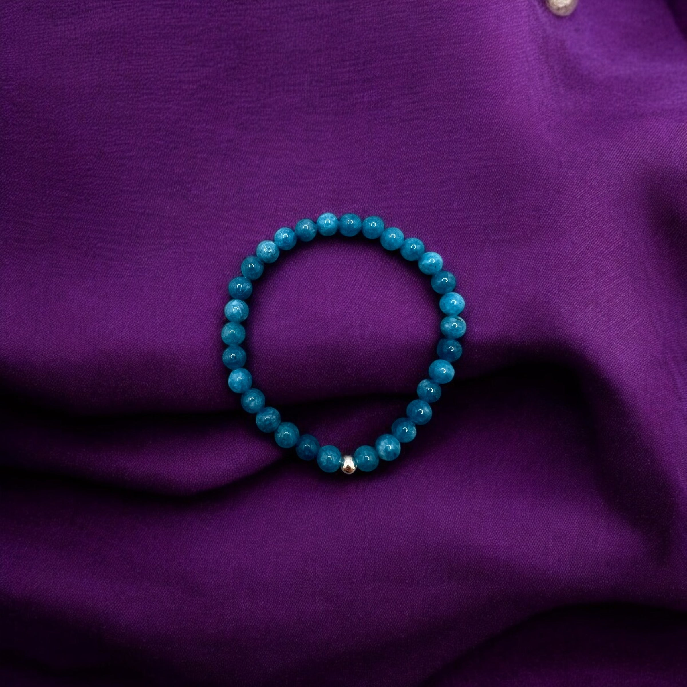 Apatit Armband with 6mm round blue beads promoting creativity and inspiration on purple fabric background