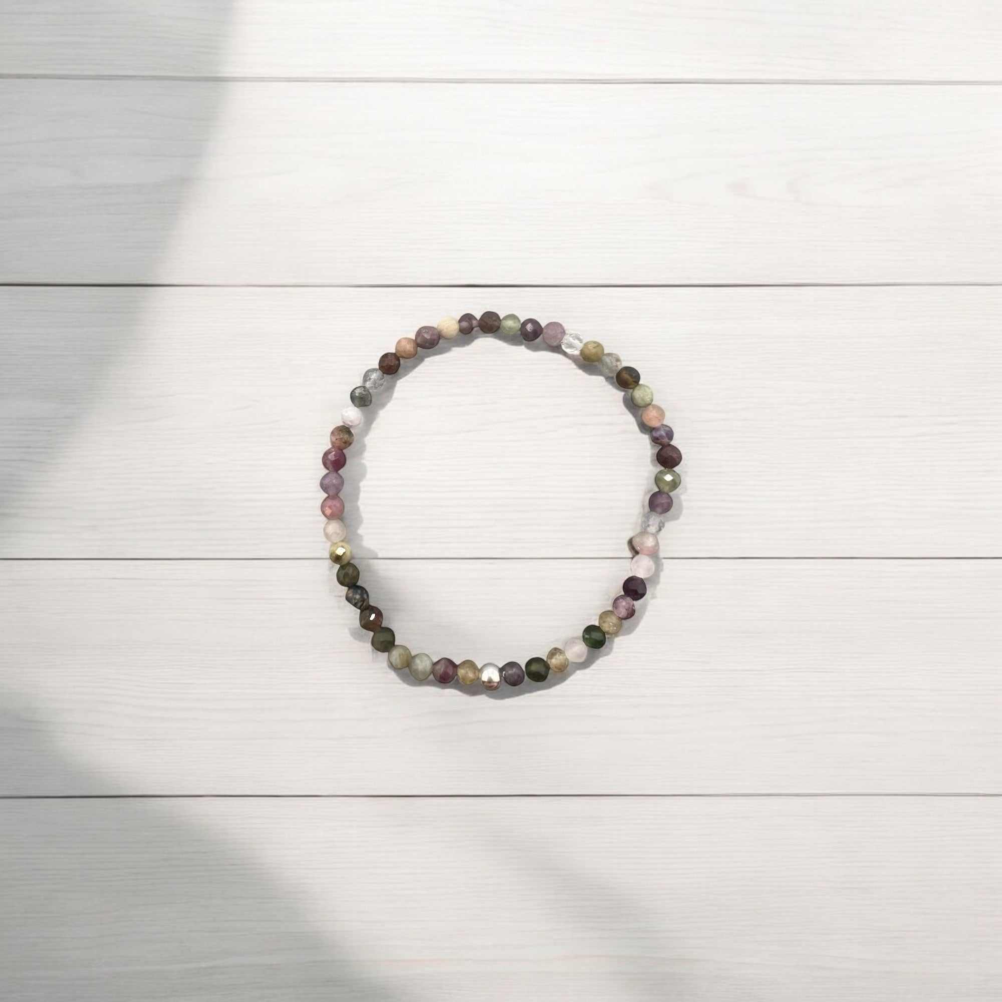 Turmalin Armband with 4mm faceted multicolored tourmaline beads for joy, love, and protection on a light wooden background